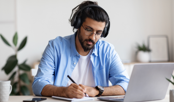 Man wearing headphones, writing at desk